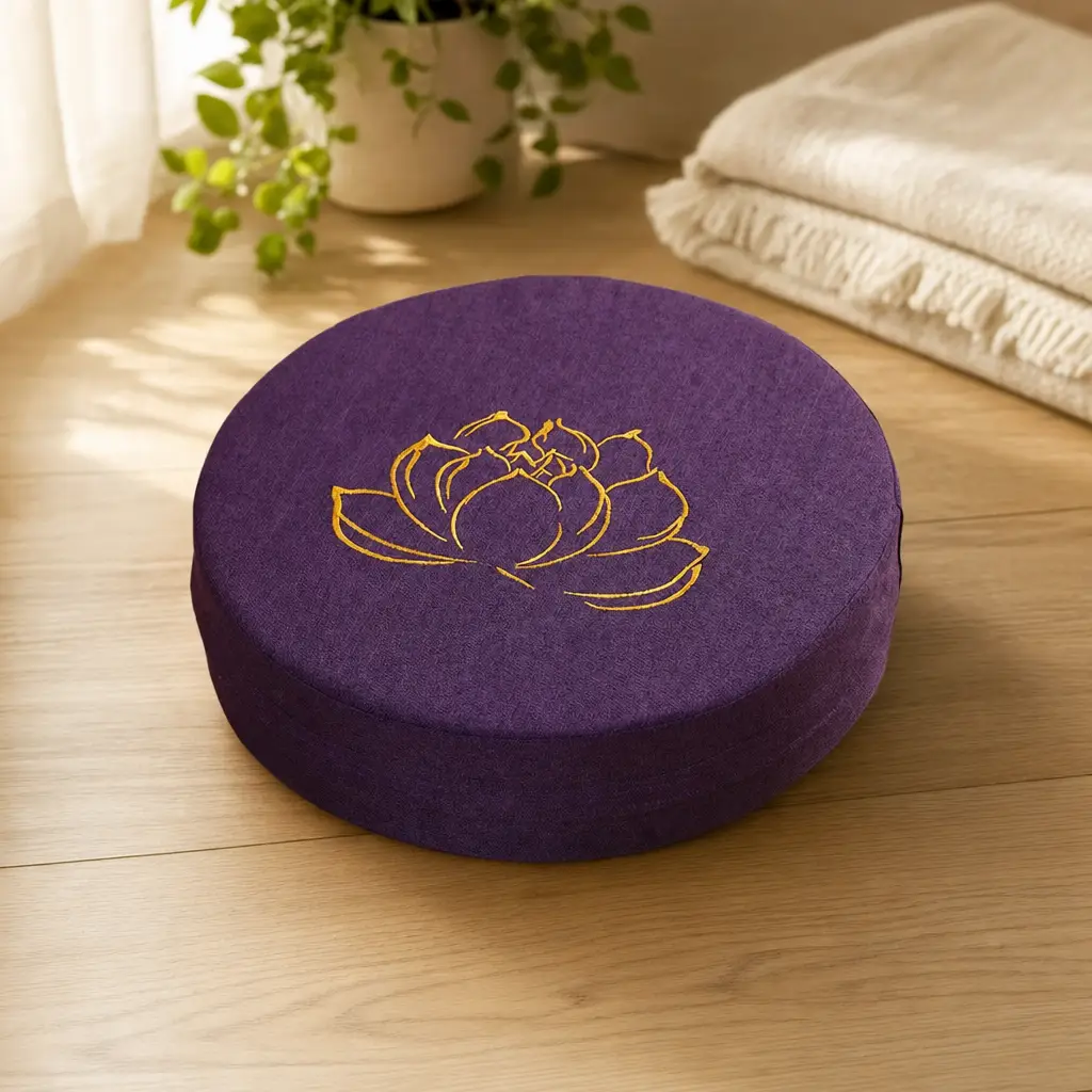 Round dark purple linen meditation cushion with gold lotus embroidery on a wood floor