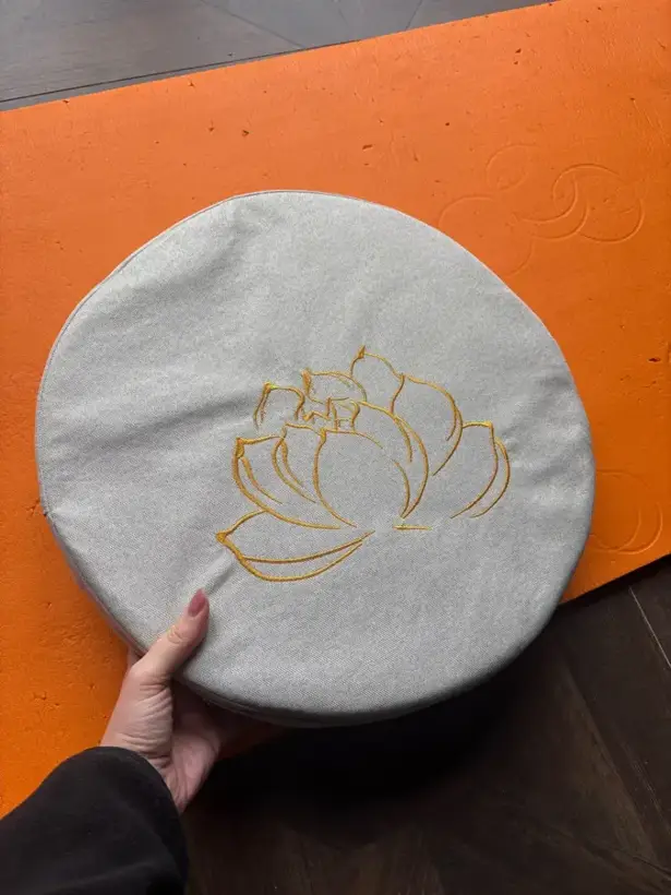 White meditation cushion placed on an orange rug, buyer photo